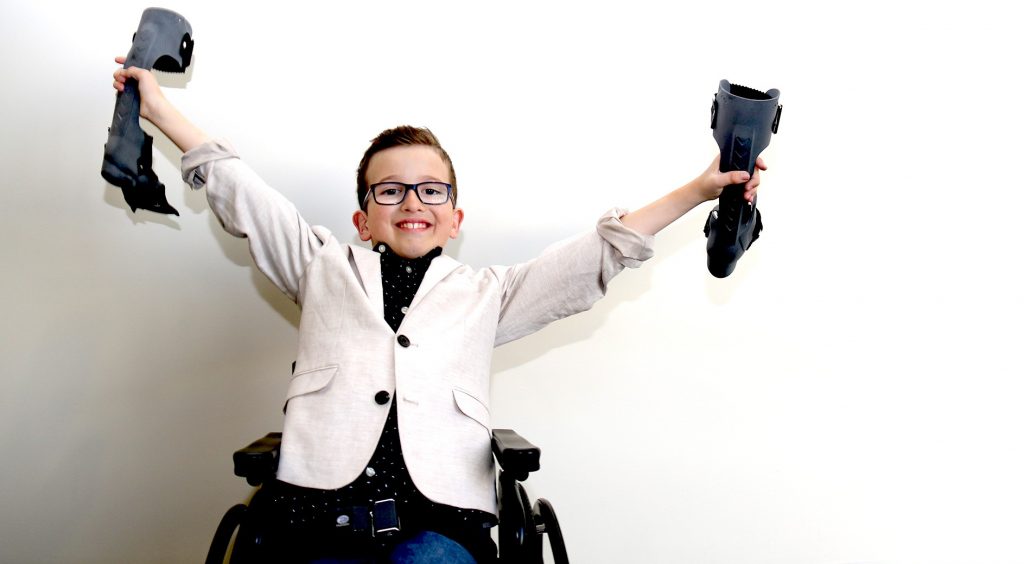 Young boy in wheelchair holding two orthotics